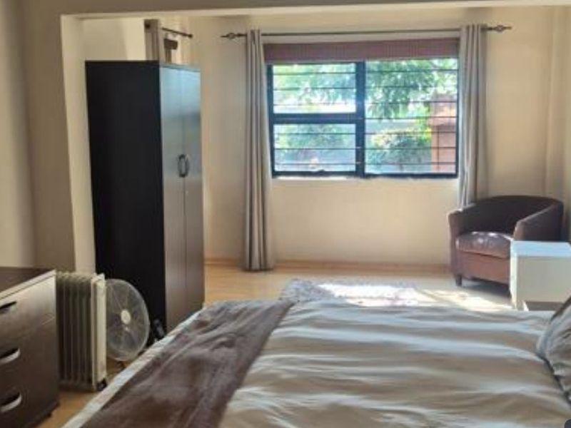 A spacious bedroom featuring laminate flooring and a large window fitted with security bars, providing natural light and a view of the exterior.
