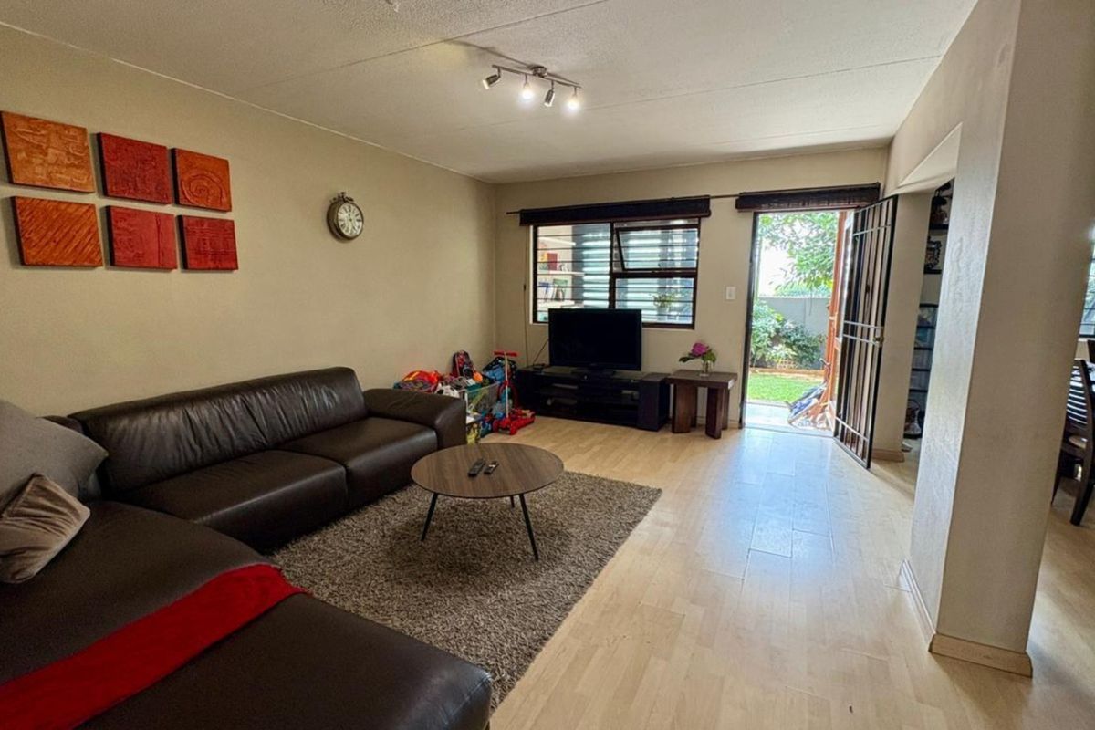 A living room featuring laminate flooring, track lighting, and direct access to an outdoor area through a security gate.