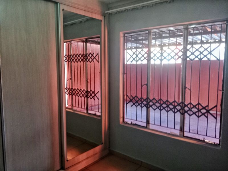 A bedroom featuring tiled flooring, a built-in wardrobe with mirrored sliding doors, and windows fitted with security bars.