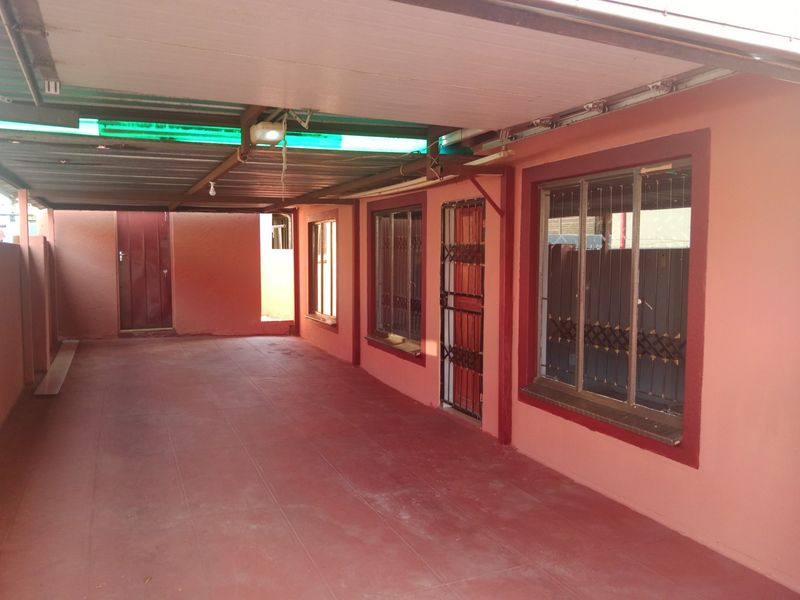 A covered outdoor patio area featuring tiled flooring, security gates, and security bars on the windows, providing a functional transition space.