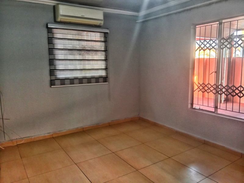 An empty living room featuring tiled flooring, a wall-mounted air conditioning unit, and security gates on the windows.