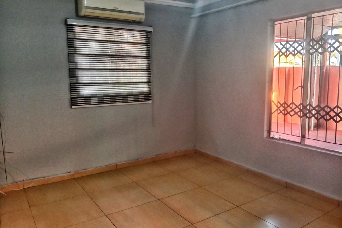 An empty living room featuring tiled flooring, a wall-mounted air conditioning unit, and security gates on the windows.