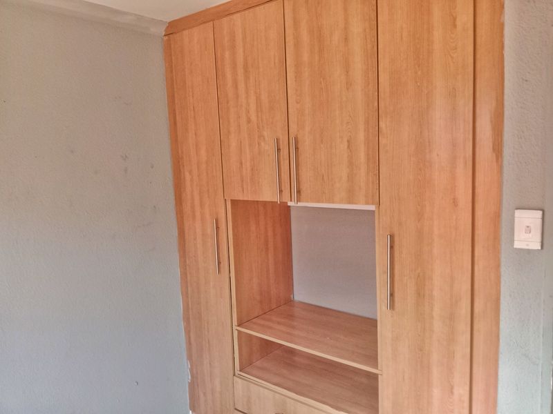 A bedroom featuring a built-in wooden wardrobe with integrated shelving and modern handles, set against a plain wall.