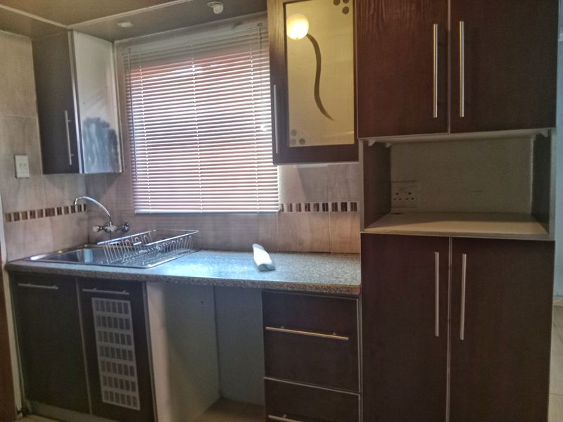A compact kitchen featuring dark wood-look cabinetry, a stainless steel sink, and tiled backsplash, offering a functional layout ready for modernization.