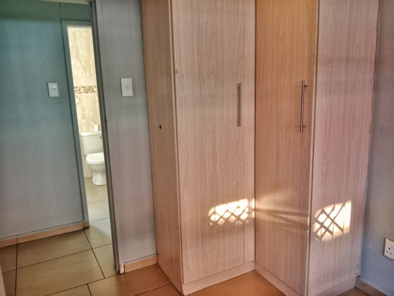 A bedroom interior featuring built-in wooden cupboards and tiled flooring, with a view into an adjacent bathroom.