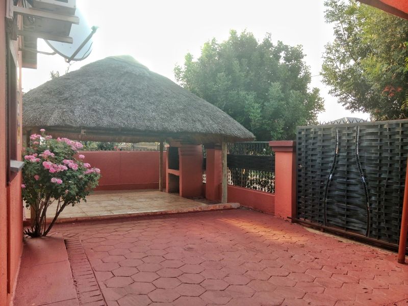 Outdoor entertainment area featuring a thatched lapa with a built-in braai, paved flooring, and secure boundary walling with a metal sliding gate.