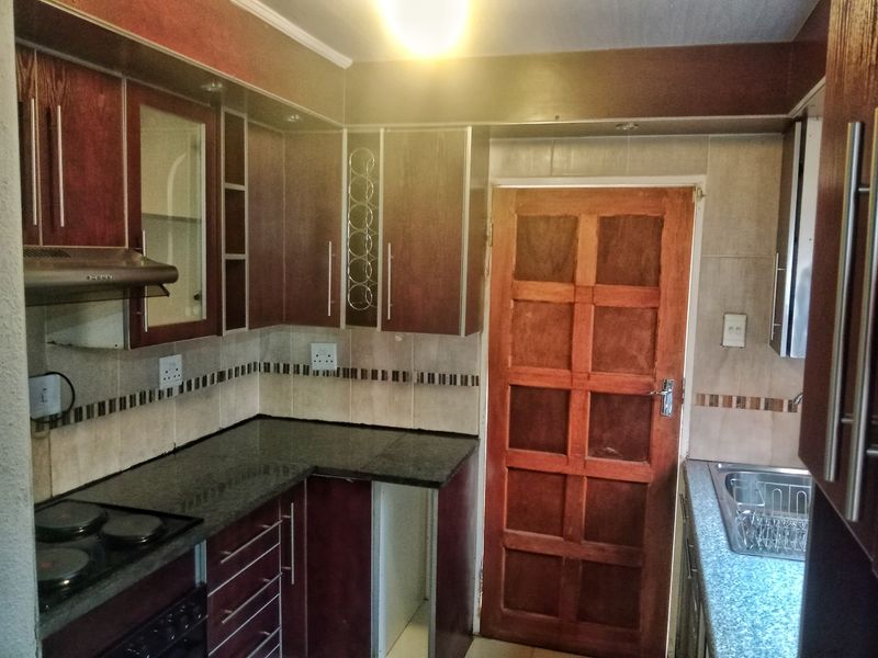 A functional kitchen featuring dark wood cabinetry, granite countertops, a built-in electric hob with extractor fan, and a tiled backsplash.