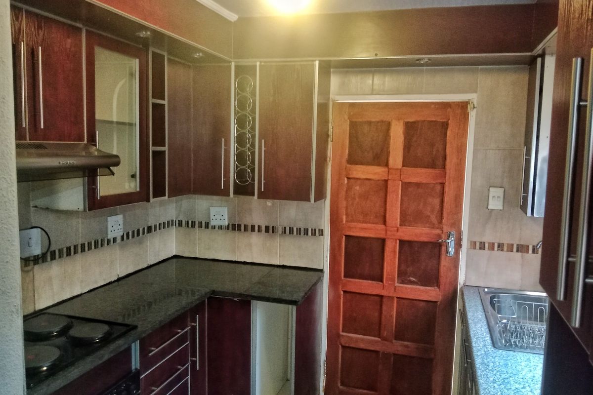 A functional kitchen featuring dark wood cabinetry, granite countertops, a built-in electric hob with extractor fan, and a tiled backsplash.