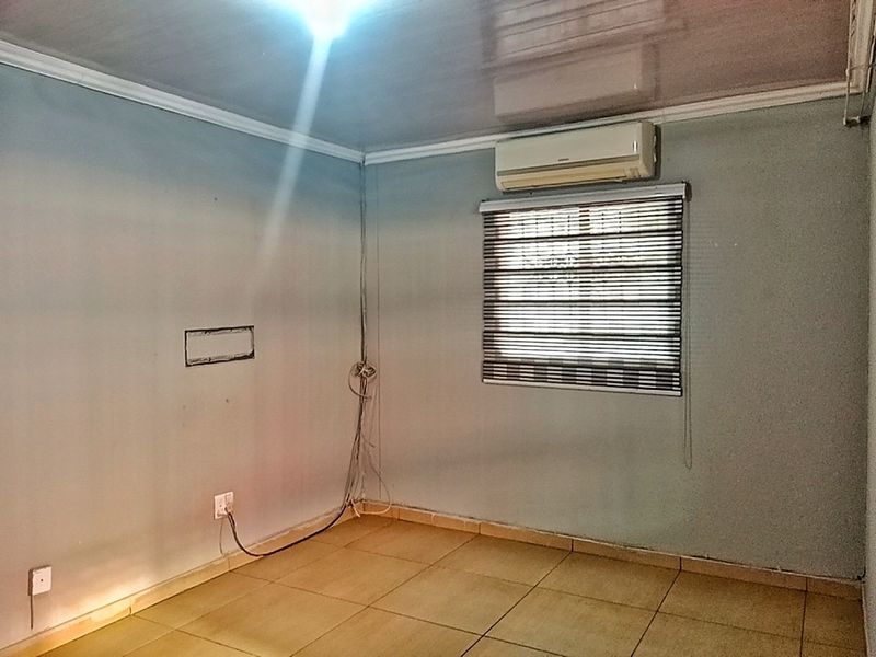 An empty bedroom featuring tiled flooring, an installed air conditioning unit, and window blinds. The space requires minor cosmetic attention to the walls and wiring.