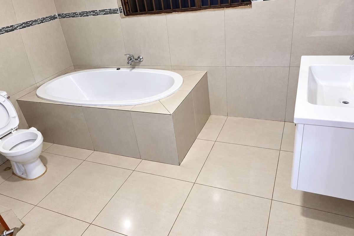 A modern, neutral-toned bathroom featuring a built-in oval bathtub, a wall-mounted vanity, and tiled finishes throughout.