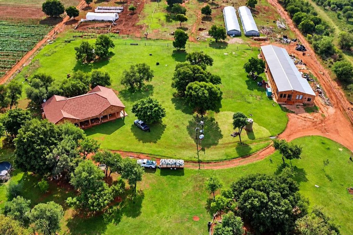Aerial view of a farm property featuring a main residence, large outbuilding, multiple greenhouses, and expansive landscaped grounds with mature trees.