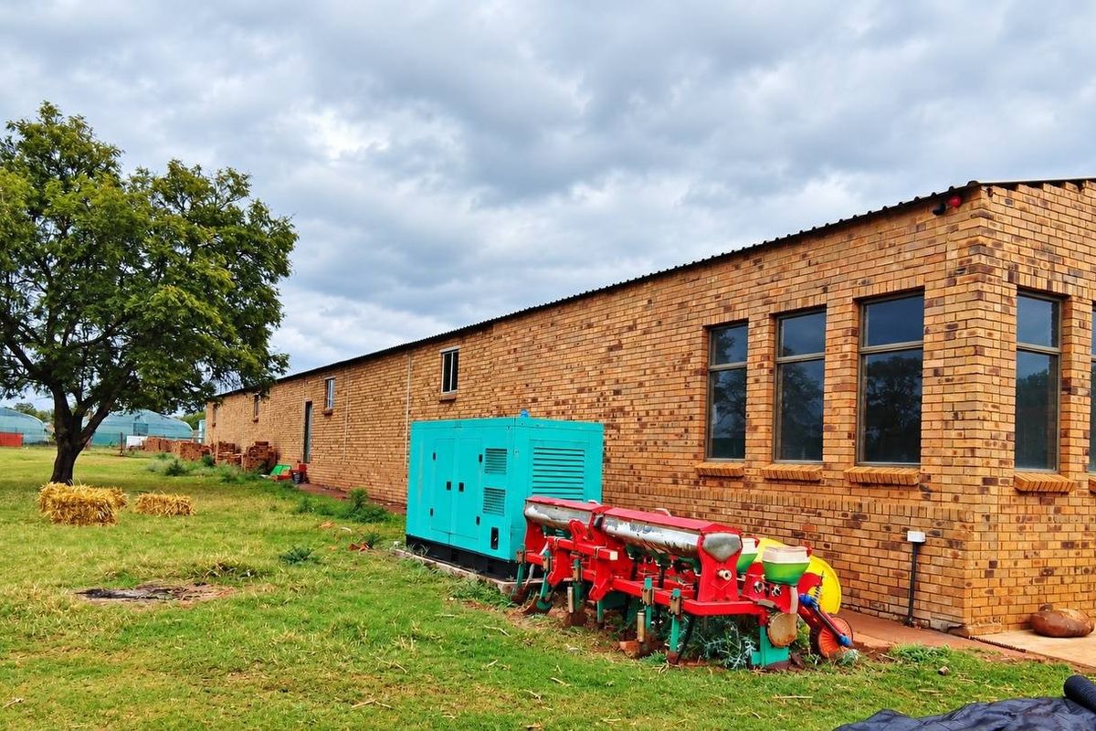 Exterior view of a long face brick farm building featuring large windows and an integrated backup generator on the property grounds.