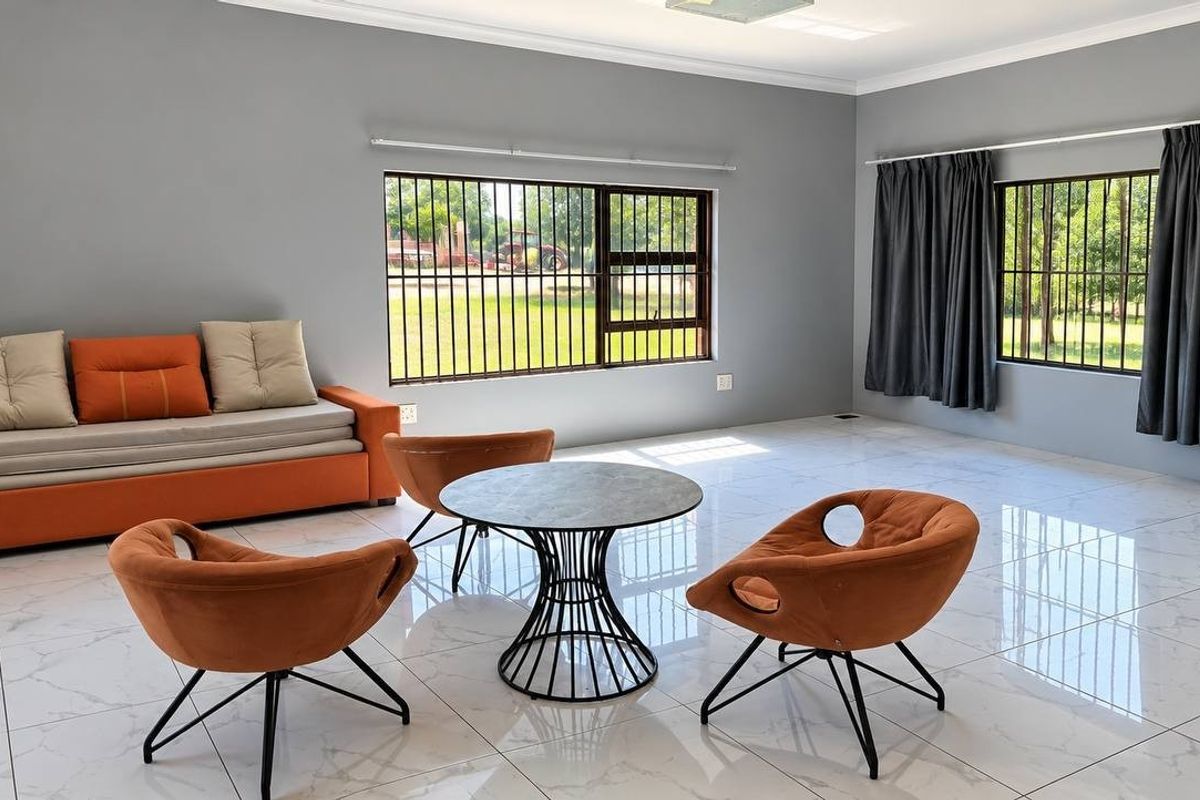 Spacious living area featuring polished porcelain tile flooring, neutral grey walls, and large windows fitted with security bars.