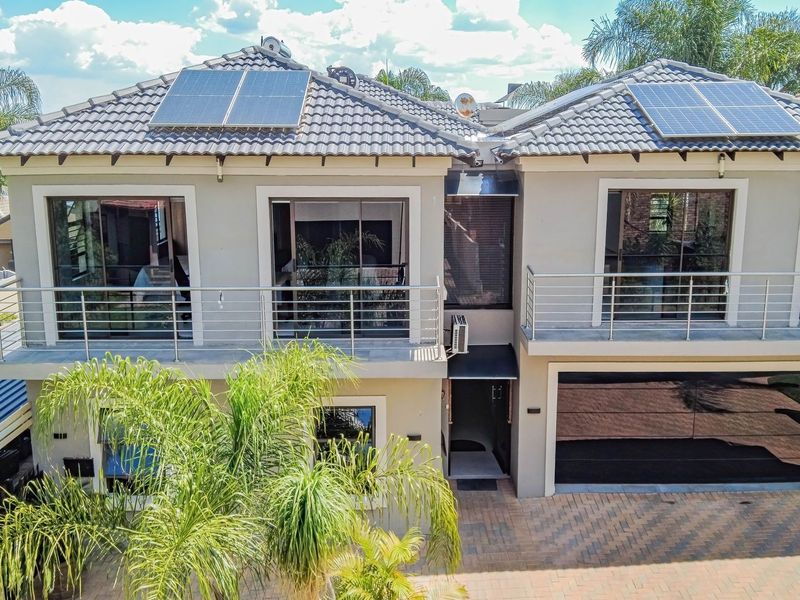 Modern double-story residence featuring a paved driveway, double garage, upper-level balconies with stainless steel balustrades, and roof-mounted solar panels.