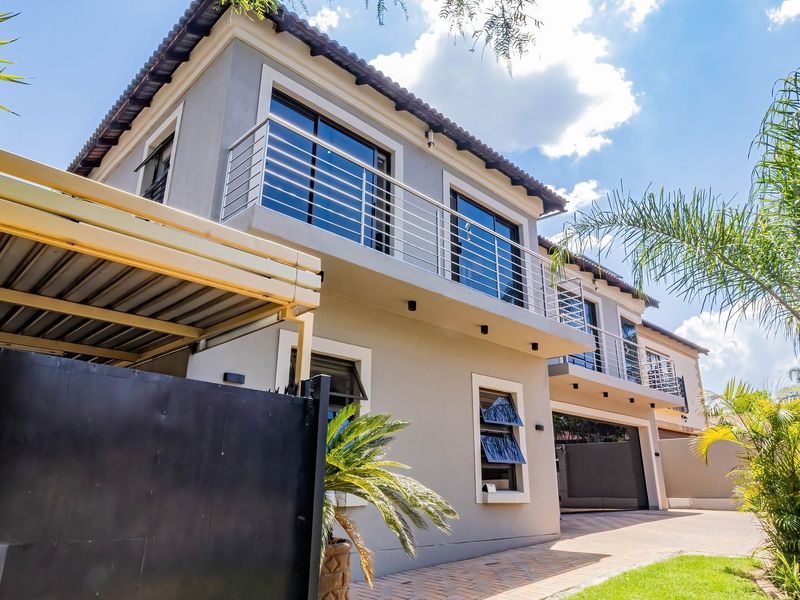 A modern double-story residential facade featuring a paved driveway, integrated carport, and upper-level balcony with stainless steel balustrades.