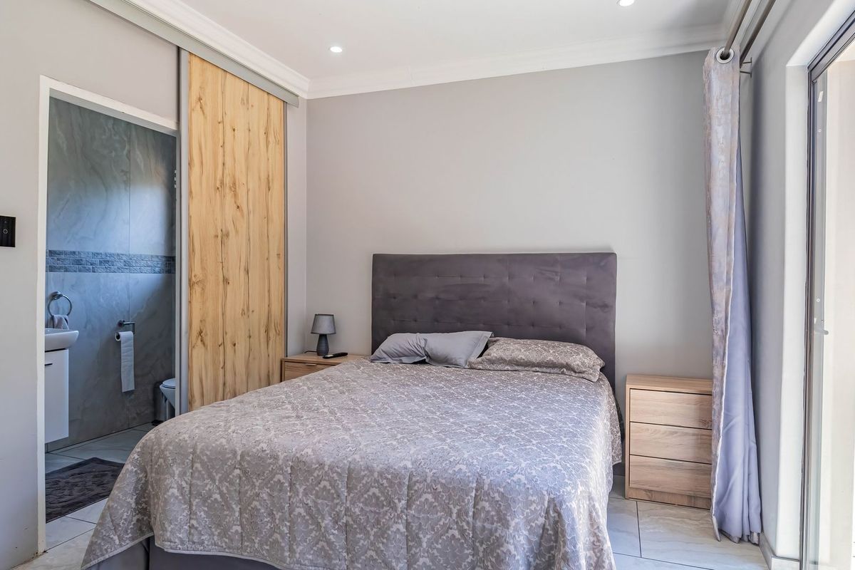 A well-maintained bedroom featuring tiled flooring, recessed lighting, a sliding barn door leading to an en-suite bathroom, and direct access to an outdoor area.