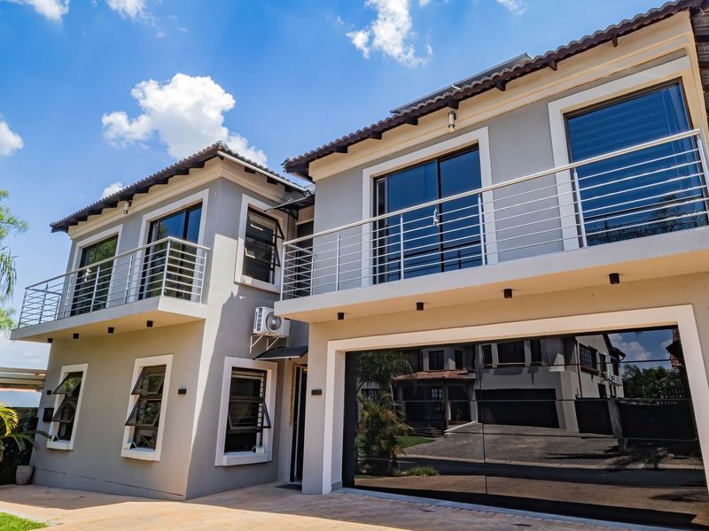 Modern double-storey residential facade featuring clean grey render, upper-level balconies with stainless steel railings, and a large automated garage door.