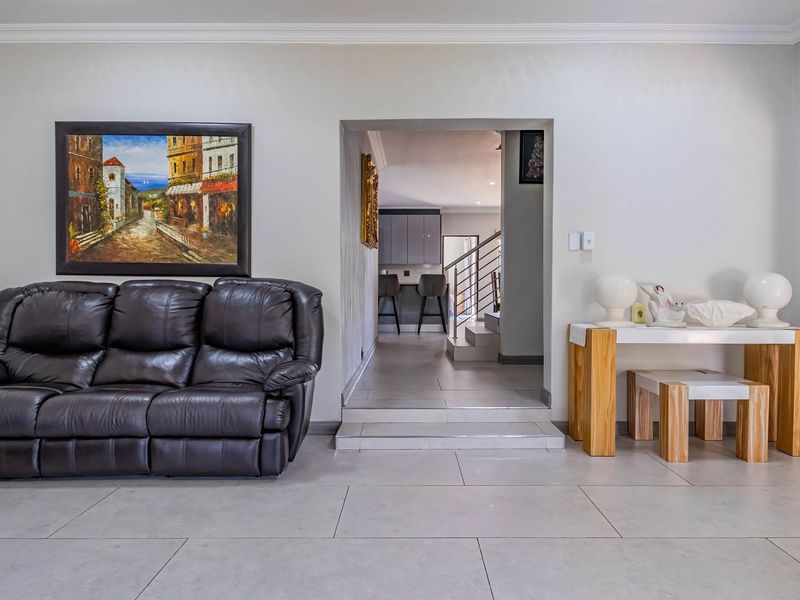 A well-maintained living area featuring neutral tiled flooring, cove cornicing, and a clear transition to an adjacent staircase and kitchen area.