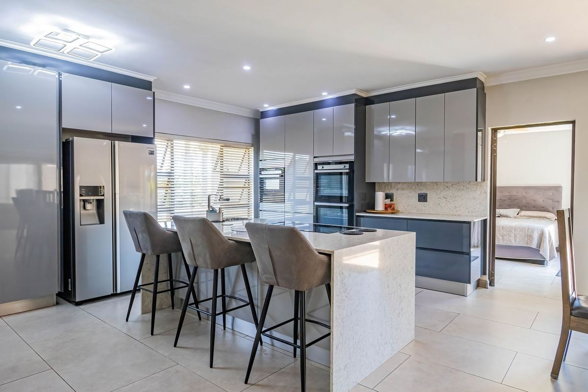 Modern kitchen featuring high-gloss cabinetry, stone countertops, a central island with breakfast bar, and integrated appliances, finished with sleek tiled flooring.