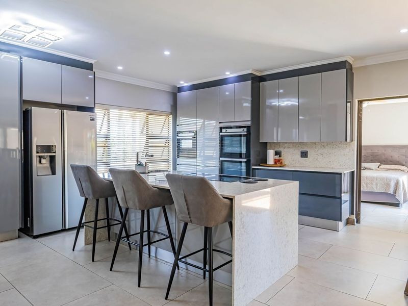 Modern kitchen featuring high-gloss cabinetry, stone countertops, a central island with breakfast bar, and integrated appliances, finished with sleek tiled flooring.
