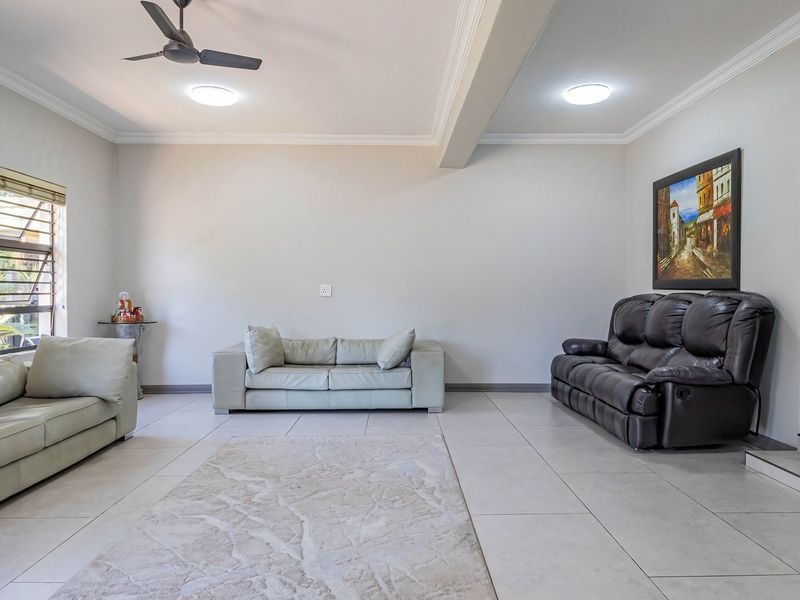 A spacious living room featuring neutral tiled flooring, crown molding, and a ceiling fan, providing a clean and versatile living space.