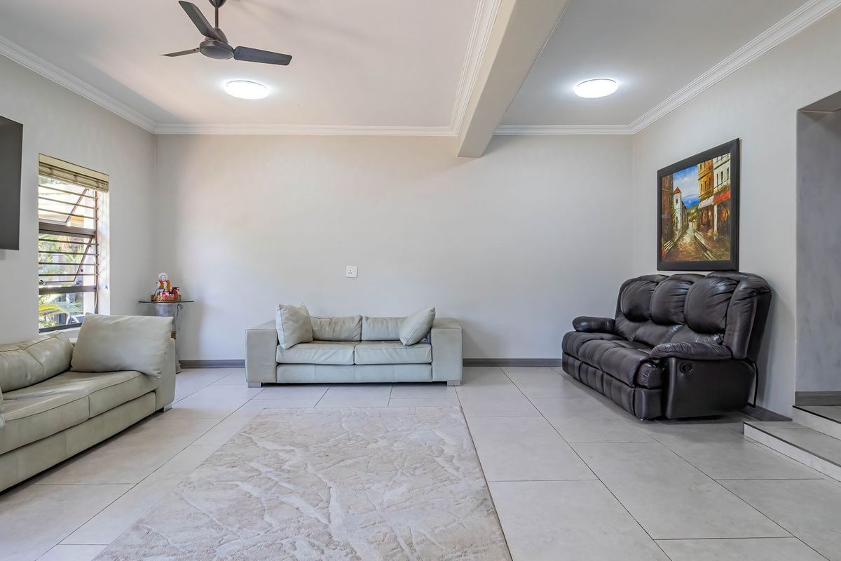 A spacious living room featuring neutral tiled flooring, crown molding, and a ceiling fan, providing a clean and versatile living space.