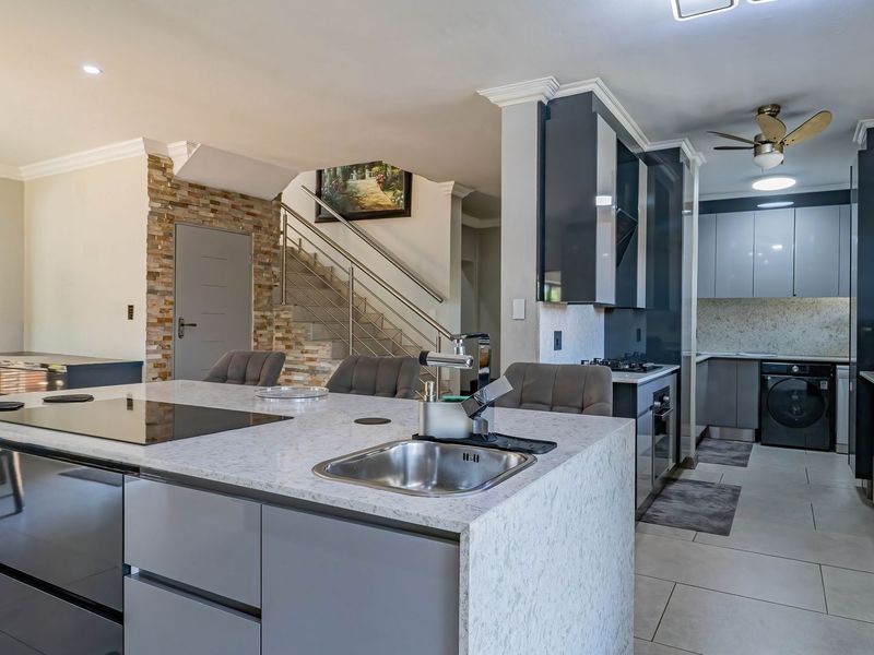 Modern open-plan kitchen featuring a large stone-topped island, sleek cabinetry, and an integrated staircase with a stone feature wall.