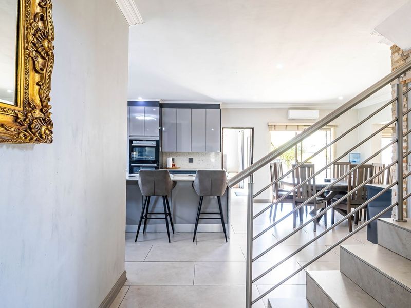 Open-plan living area featuring a modern kitchen with built-in appliances, tiled flooring, and a staircase with a contemporary stainless steel balustrade.