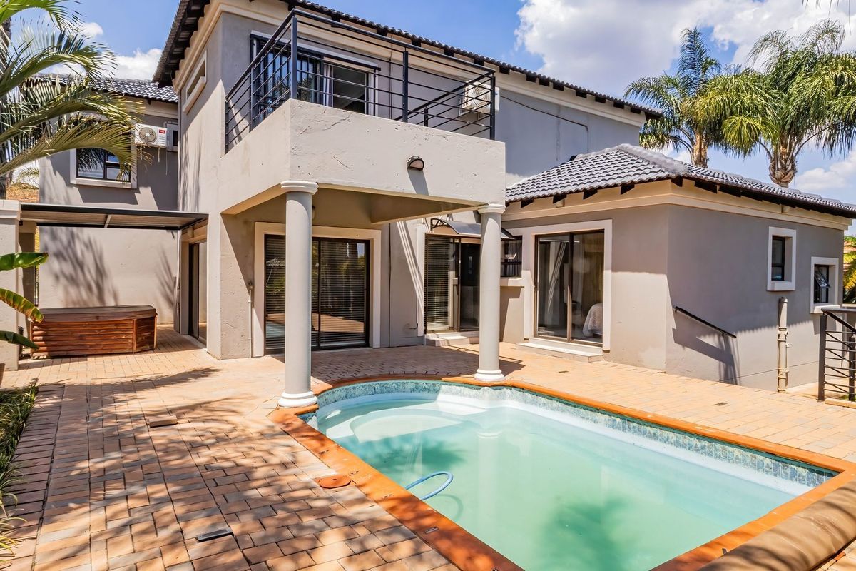Rear view of the property featuring a paved patio area, a swimming pool, and an upper-level balcony with metal railings.
