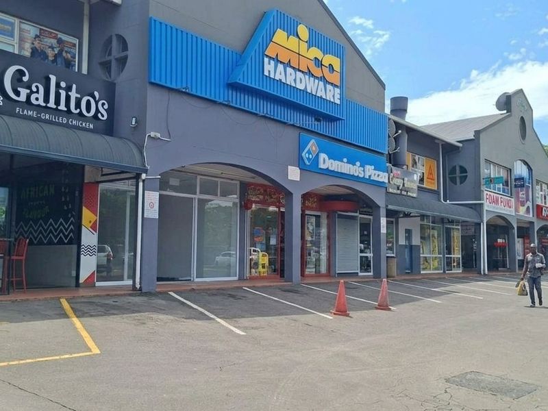 A commercial retail strip center featuring multiple storefronts with signage, glass facades, and an asphalt parking area in front.
