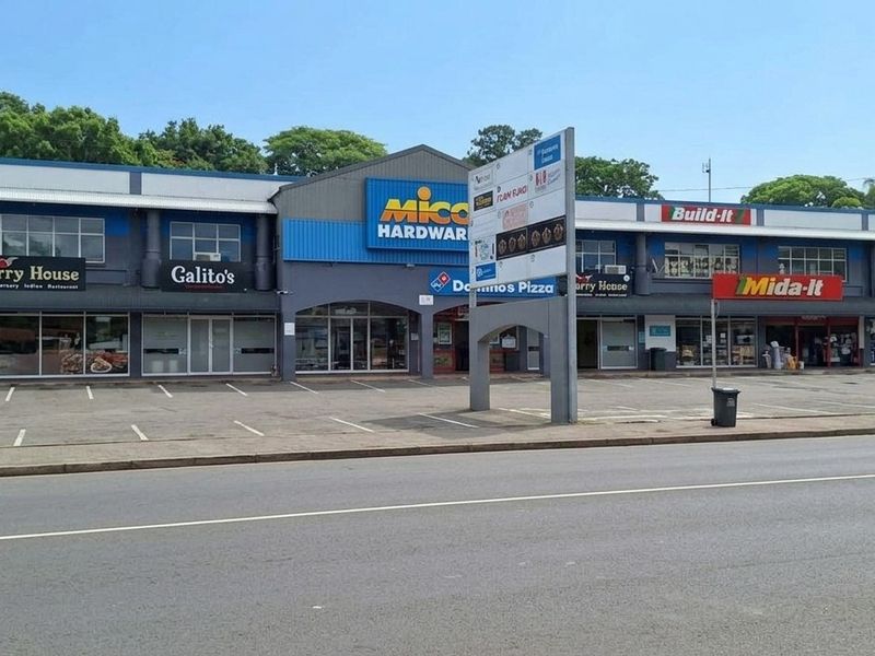 Front view of a commercial retail strip center featuring multiple storefronts, covered walkways, and an asphalt parking area.