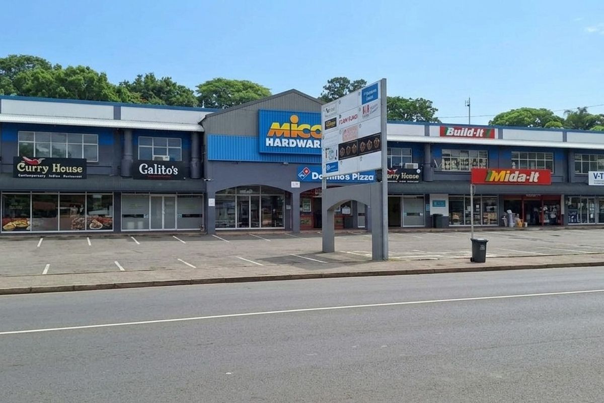 Front view of a commercial retail strip center featuring multiple storefronts, covered walkways, and an asphalt parking area.