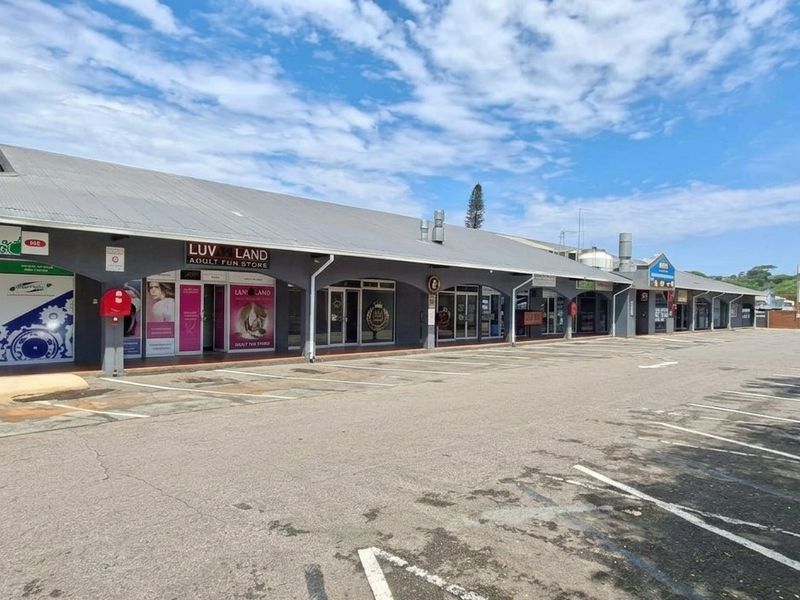 A commercial strip mall featuring multiple storefronts with a covered walkway and an adjacent asphalt parking area.
