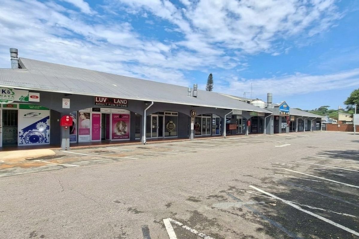 A commercial strip mall featuring multiple storefronts with a covered walkway and an adjacent asphalt parking area.