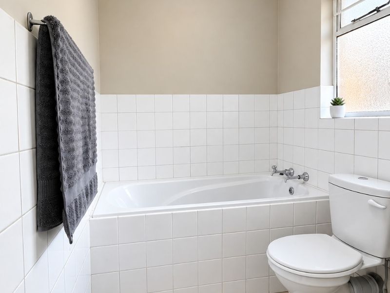 A functional bathroom featuring a built-in bathtub, standard toilet, tiled flooring, and wall tiling, offering a clean and neutral space.