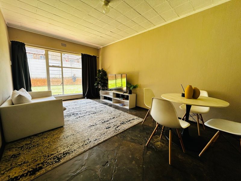 Open plan living and dining area featuring polished concrete floors, textured ceiling tiles, and large windows providing natural light and garden views.