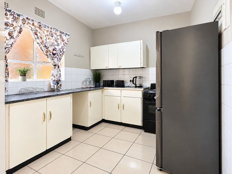 A functional kitchen featuring tiled flooring, a tiled backsplash, laminate countertops, and built-in cabinetry with a freestanding stove.