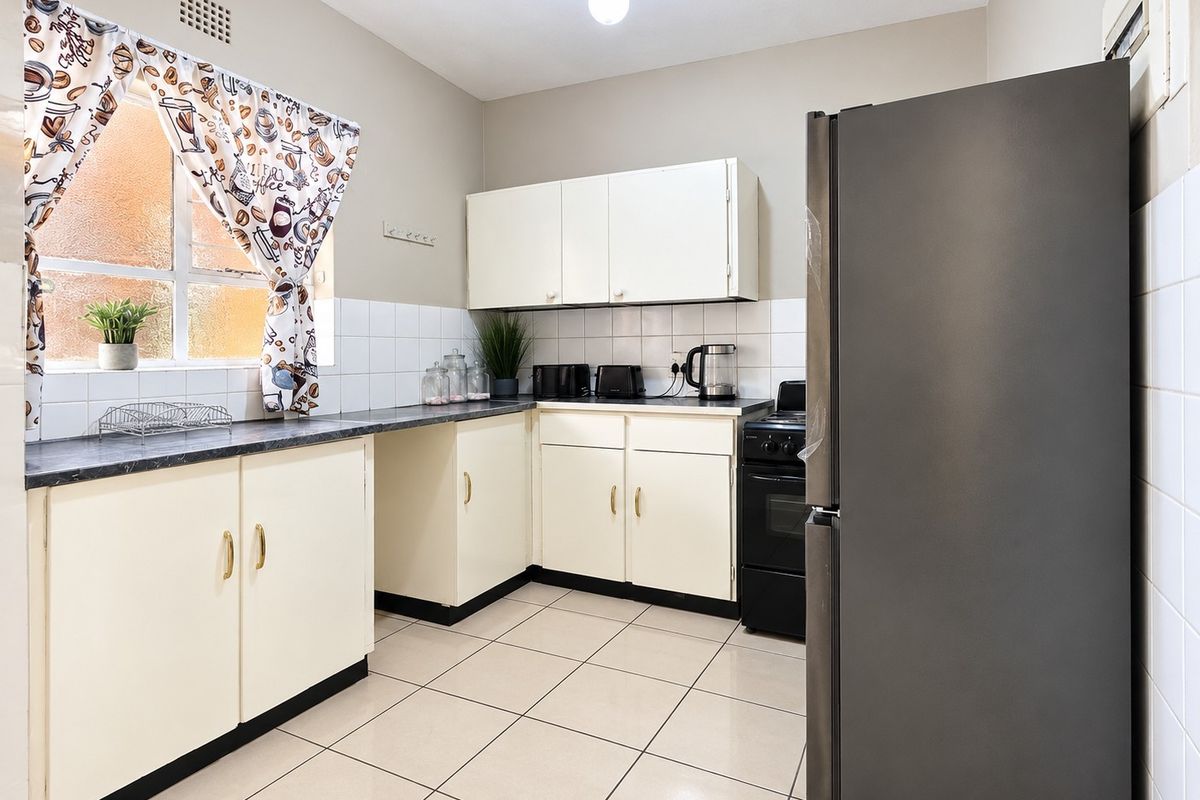 A functional kitchen featuring tiled flooring, a tiled backsplash, laminate countertops, and built-in cabinetry with a freestanding stove.