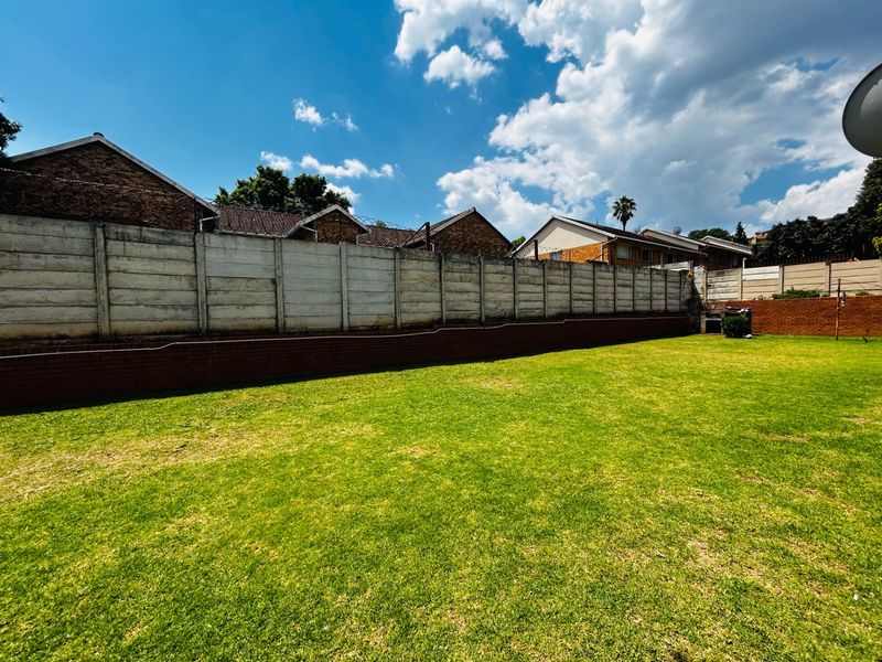 A spacious, well-maintained lawn area enclosed by a precast concrete boundary wall and a low brick retaining wall.