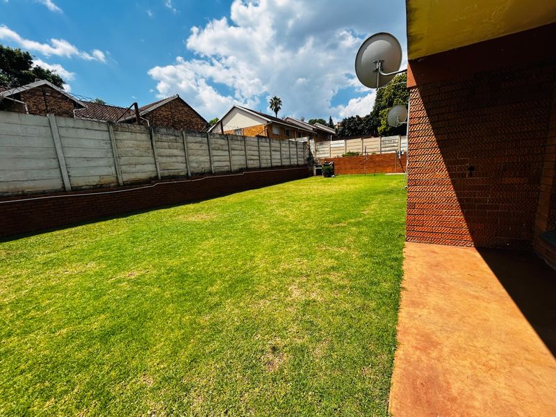 A spacious private garden featuring a well-maintained lawn, enclosed by precast concrete and brick boundary walls with a paved patio area.