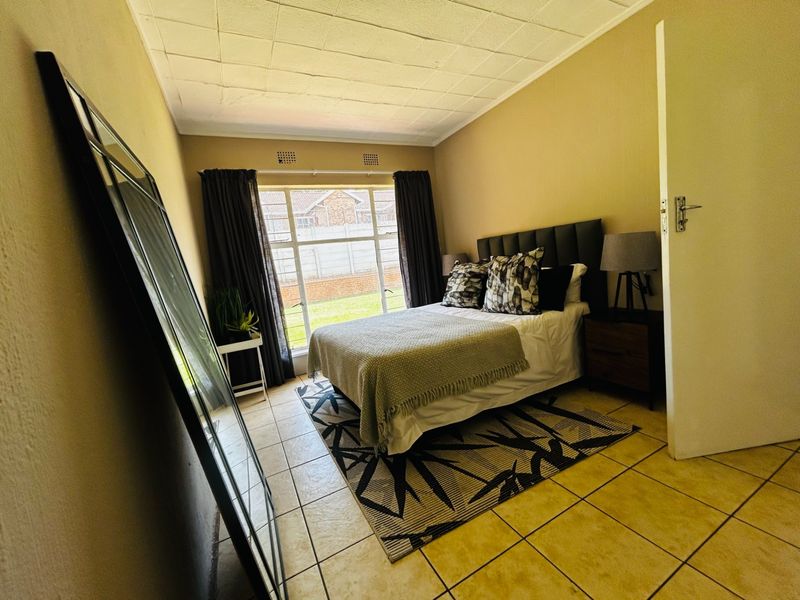 A bedroom featuring tiled flooring, a large window providing natural light, and a textured ceiling finish.
