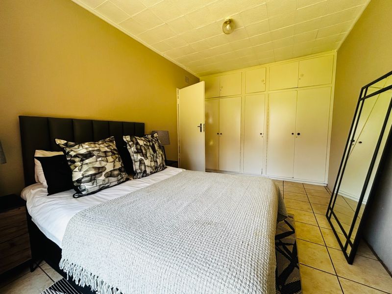 A bedroom featuring built-in cupboards, tiled flooring, and a textured ceiling finish.