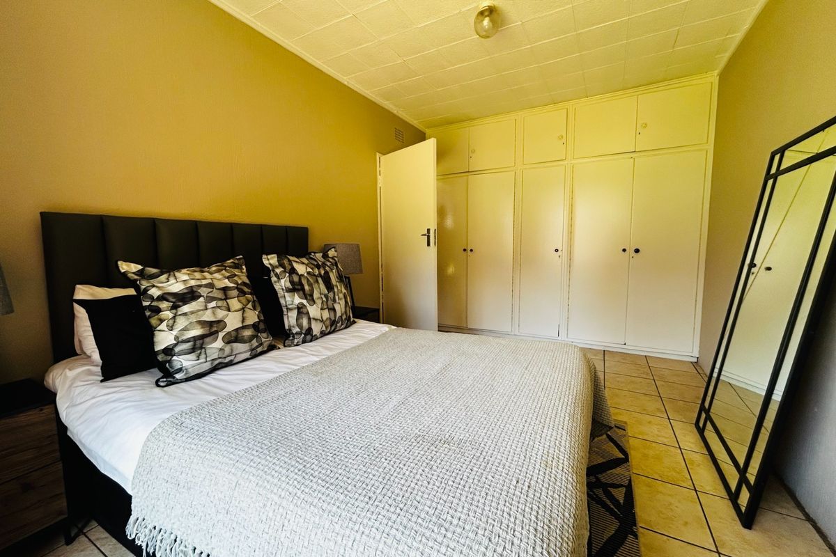 A bedroom featuring built-in cupboards, tiled flooring, and a textured ceiling finish.