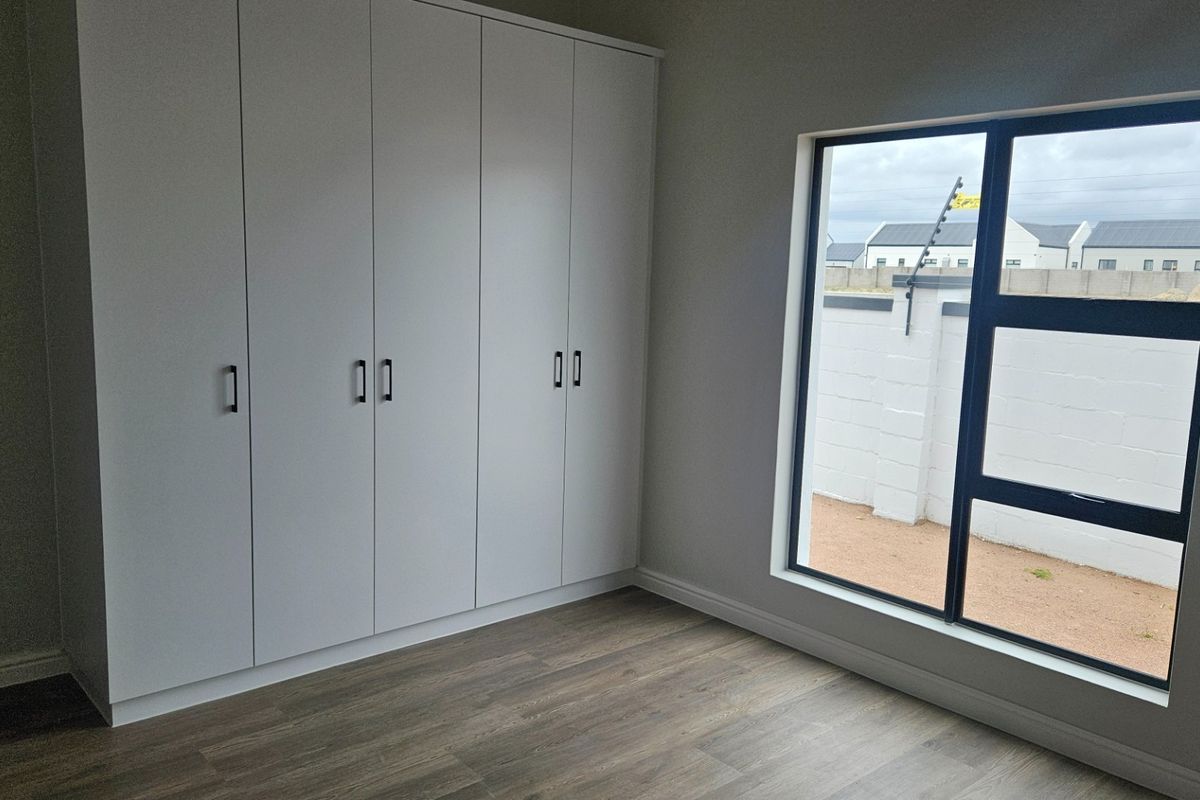 A bright, modern bedroom featuring neutral walls, high-quality laminate flooring, and ample built-in cupboard storage space.