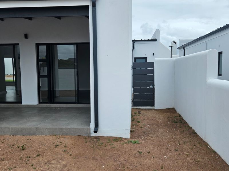A modern rear exterior view featuring a covered patio with tiled flooring, sliding glass doors, and a secure side gate with boundary walling.