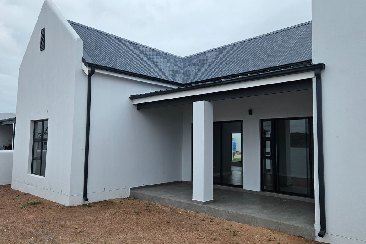 A modern rear exterior view of the house featuring a covered patio with tiled flooring, sliding glass doors, and a clean white facade.