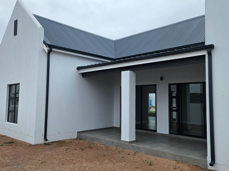 A modern rear exterior view of the house featuring a covered patio with tiled flooring, sliding glass doors, and a clean white facade.