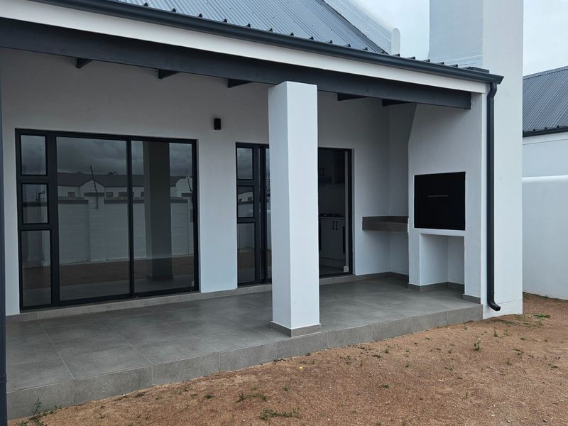 A modern covered patio featuring tiled flooring, a built-in braai, and sliding glass doors providing seamless access to the interior living space.