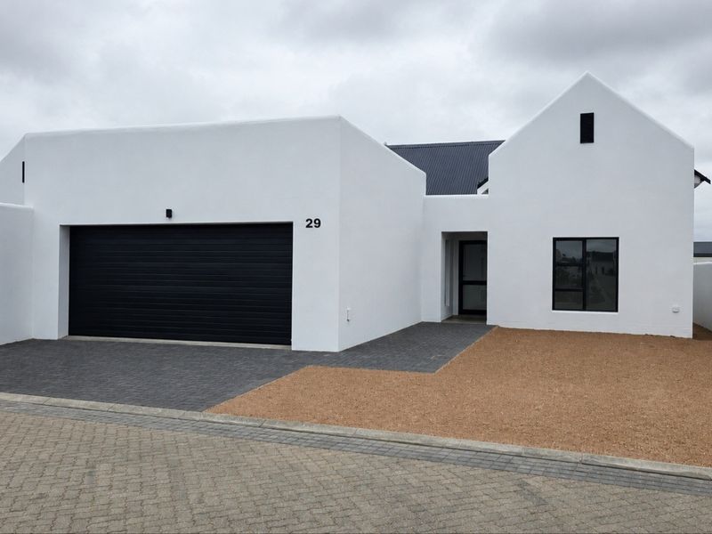 Modern single-story home featuring a clean white facade, black garage door, and minimalist architectural design with a paved driveway and gravel landscaping.