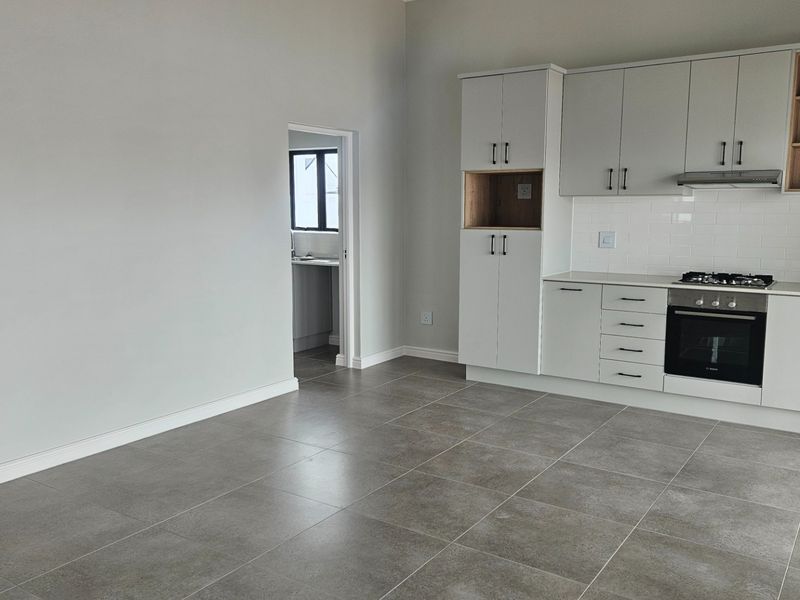 Modern open-plan kitchen featuring sleek white cabinetry, integrated gas hob, electric oven, extractor fan, and stylish subway tile backsplash with neutral tiled flooring.